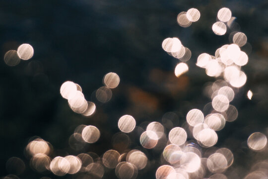 Backlit bokeh light spots on the water surface, a dreamy background of circular light and shadow.