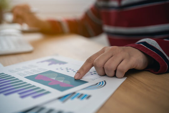 Person analyzing business chart report data with finger pointing on graph paper on wooden desk in office workspace