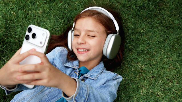 Happy redhead girl taking selfie photos with smartphone and headphones on grass - Technology, music and social media lifestyle concept