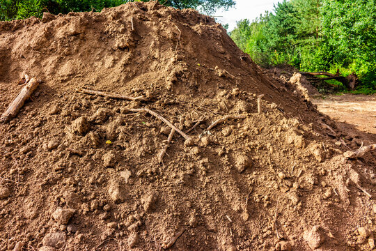 Large pile of brown soil excavated during earthworks with scattered roots and dirt clods, creating a rugged texture at an active construction or landscape development site