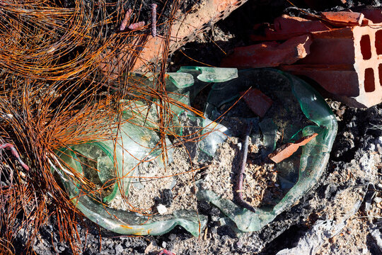 Burnt tire cord and melted glass jar among debris and ash, rusty wire remnants from old tires, ecological damage and toxic waste from illegal trash burning