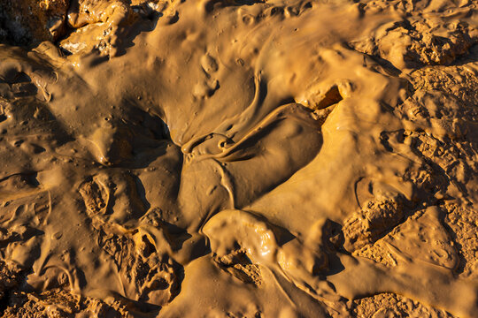 Thick textured wet clay sludge glistening in an open pit, organic earthy substance creating a dangerous mire, natural therapeutic mud background with detailed soil ripples and gooey surface