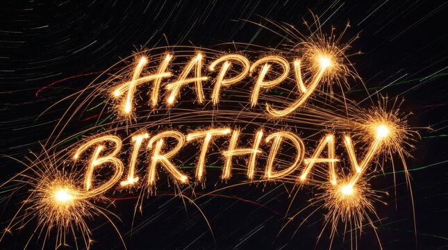 Happy Birthday text written with glowing bright sparklers on a dark night background.