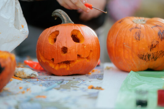 Carving Halloween Pumpkins At A Creative Workshop Table Close Up. Close up of a hand carving spooky jack o lantern face into an orange pumpkin
