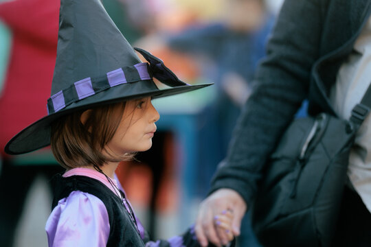 Little Girl In Witch Costume Holding Hands At Halloween Festival. Side view of a cute young girl wearing a black witch hat during an autumn celebration
