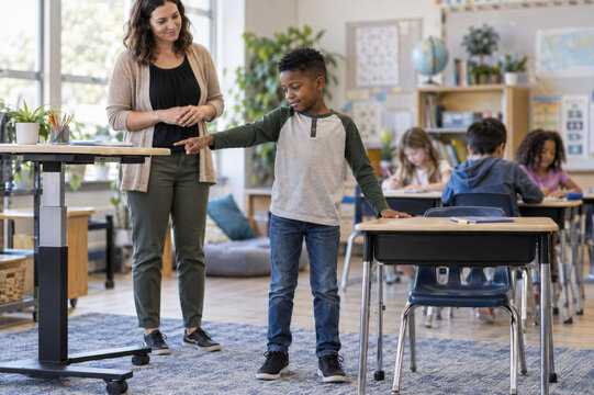 Teacher supporting schoolboy pointing across classroom. ADHD awareness and inclusive education. Individual learning support and student engagement. Elementary classroom assistance