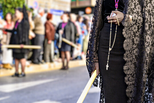 A woman dressed in traditional manola attire (with a black mantilla), holding a rosary and a large candle during a Holy Week procession in Granada, Andalusia, Spain.