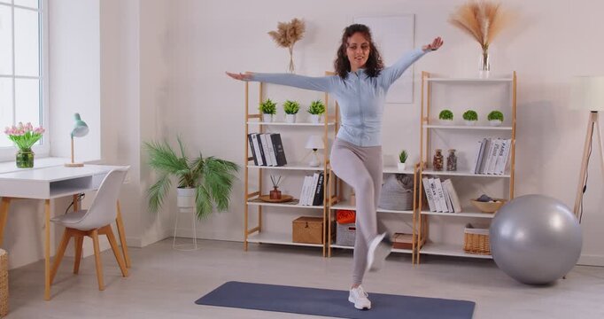 Young woman in sports wear doing exercises on fitness mat at home, raising legs to hands during training. Focused active female practicing stretching, improving balance flexibility and core strength.
