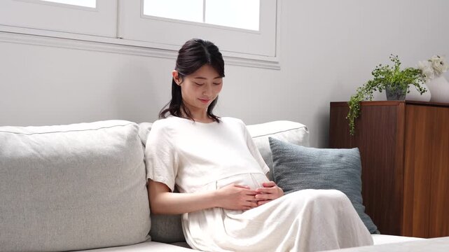 ソファーに座ってお腹を触る妊婦