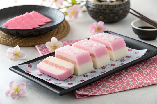Pink and white layered rice cake dessert served on a black plate with cherry blossoms