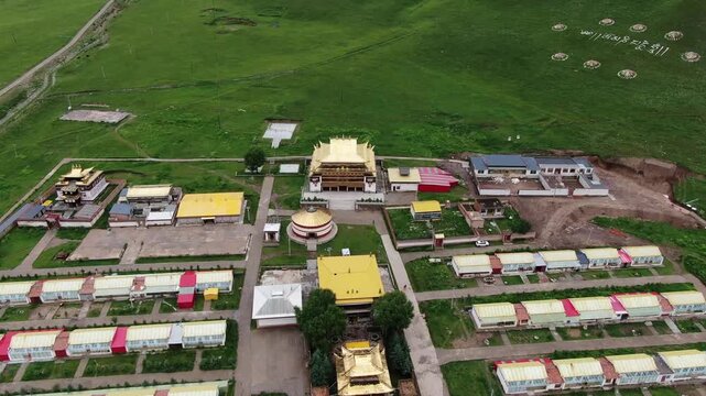 Aerial drone view of Aru Monastery in Qilian Mountains, Qinghai, with golden-roofed temples, prayer wheels, and surrounding grassland monastery complex