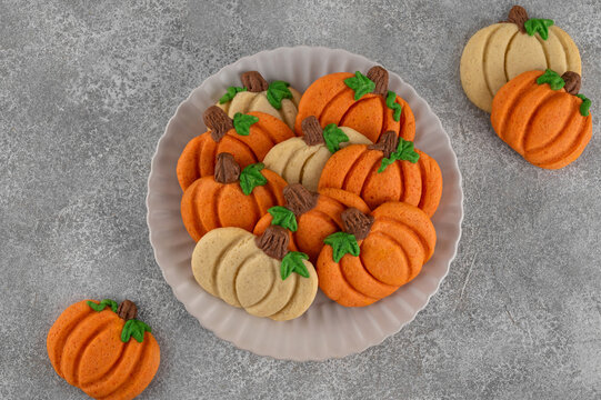 Themed dessert for Thanksgiving. Spiced cookies in the shape of white and orange pumpkins on a plate on a concrete background. Top view, copy space.