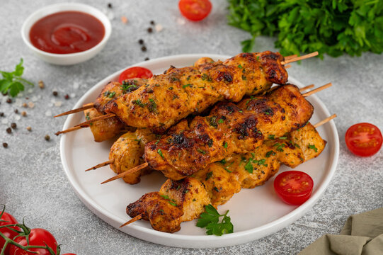 Juicy chicken skewers cooked in an air fryer and served on a plate with fresh herbs, cherry tomatoes and dipping sauce. Healthy food. Top view, copy space.