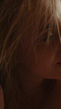 Beautiful vertical macro of the face of an attractive blonde woman playing with her hair and shaking her head in slow motion
