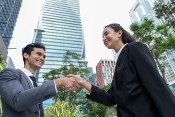 Two business partners in formal suits greeting each other with a handshake at the foot of a glass skyscraper, a documentary style view of professional life in the city © ultramansk