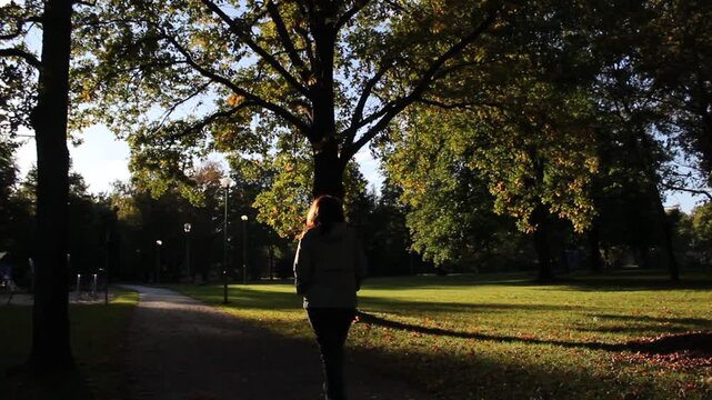 Woman Walking on Path in City Park Backlight.

