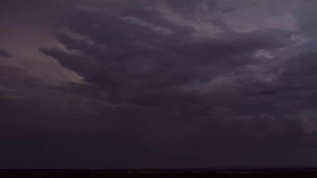 Dark storm clouds rolling across the open sky at dusk with faint horizon glow