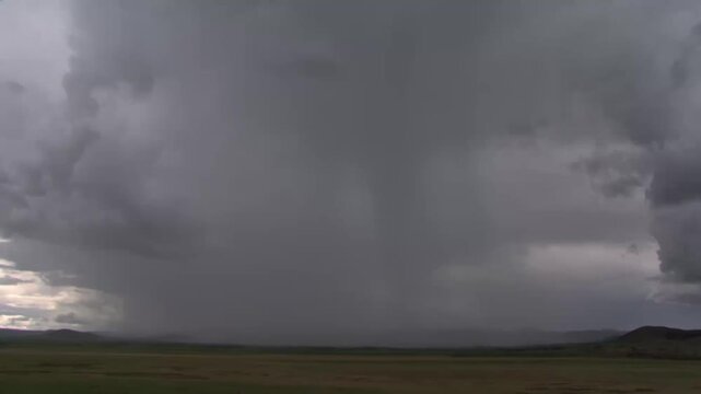 Dark storm clouds rolling across open plain at dusk with rain shafts and distant, storm front