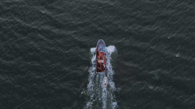 Aerial drone view of a fishing boat navigating dark ocean waters with a smaller support vessel trailing behind, creating white wake patterns