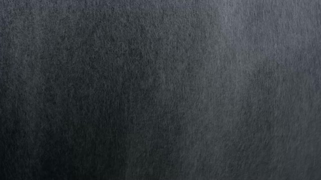 Close-up of raindrops falling on wet asphalt road surface with motion blur and textured detail
