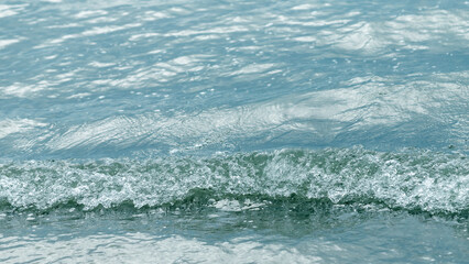Gentle blue  waves ripple across the water surface, creating textured movement and subtle reflections. Calm marine scene ideal for backgrounds, nature projects, travel and summer themes. © lms_lms