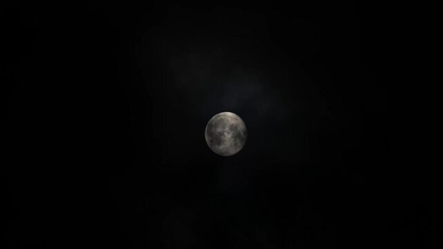 Full moon glowing in night sky with drifting clouds captured from a steady high-angle fixed camera perspective