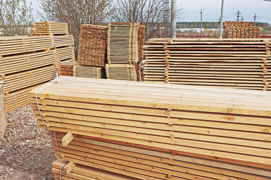 Stacked lumber boards and wooden pallets at open sawmill yard. Horizontal planks tied with white strap. Industrial wood storage