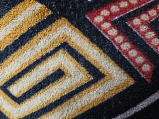 Close-up of a carpet surface showing a repeating woven pattern and detailed textile texture. © Aditya