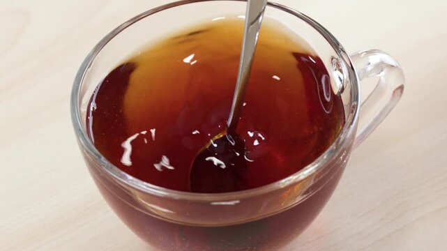 Stirring Hot Black Tea in a Clear Glass Cup with Spoon