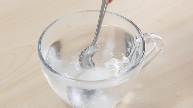 Person Stirring Clear Water in Glass Cup with Metal Spoon