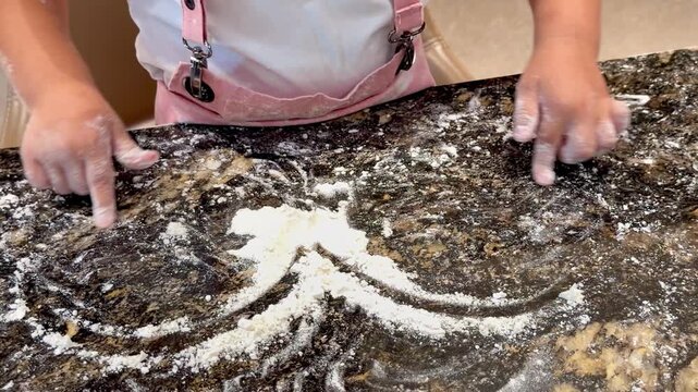 &mdash; A child's hands draw a heart in the flour scattered across a dark stone countertop &mdash; close-up, 16:9.