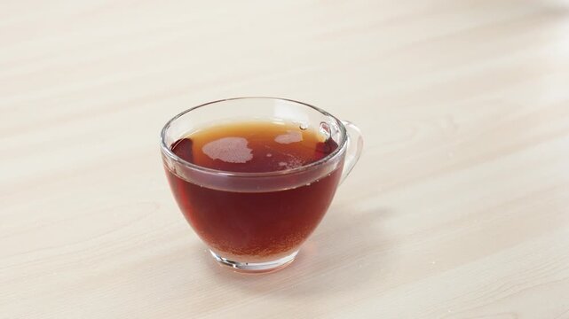 Pouring White Sugar into a Clear Glass Cup of Hot Black Tea