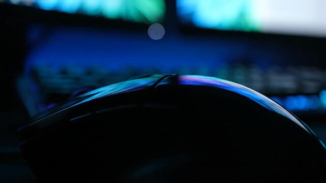 A computer mouse with colorful lights reflects while someone plays a video game in a dark room