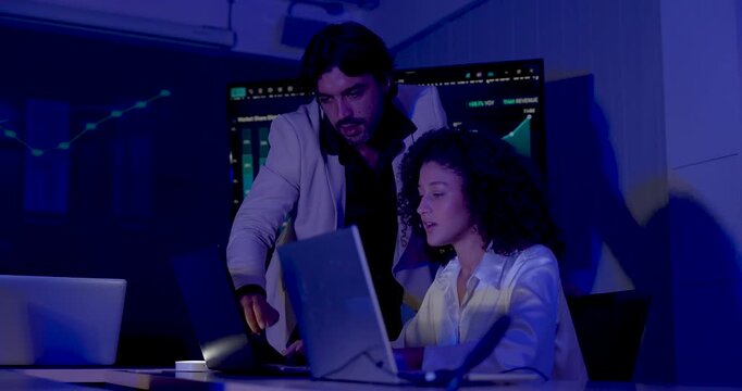 Adult female analyst reviews laptop with male manager, then both turn toward performance dashboard as manager points at chart, discussing business intelligence and data driven corporate strategy.