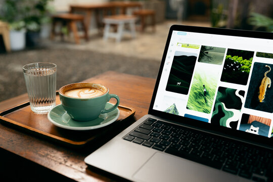 Remote work lifestyle, laptop screen showing photos with a cup of hot coffee on rustic wooden table.