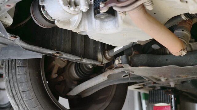 Used engine oil draining from the underside of a car during an oil change and routine vehicle maintenance service.