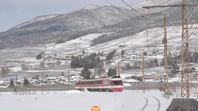 雪に覆われた山麓と集落を走る長野電鉄の特急ゆけむり（1000形）の俯瞰映像