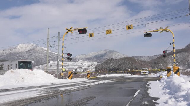 晴天の青空と雪山の麓の踏切を通過する長野電鉄のローカル電車