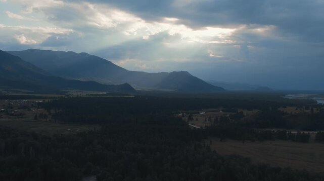 Drone footage of a wide mountain valley with a winding river, forest patches and fields under dramatic storm clouds near Zamulta village, Altai Republic, Russia