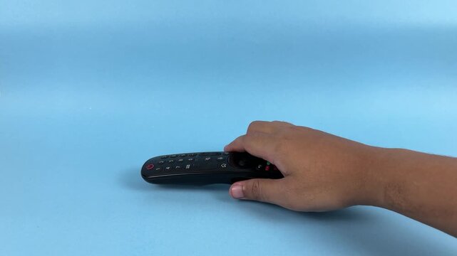 Hand Holding TV Remote Control Pointing Forward on Blue Background