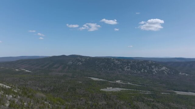 Drone footage of mountain ridge and vast taiga forest under blue sky with clouds in Taganay National Park near Zlatoust, Chelyabinsk Oblast, Russia