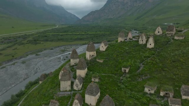 Drone footage of the Dargavs necropolis known as the City of the Dead on a green hillside above a river valley in North Ossetia&ndash;Alania, Russia