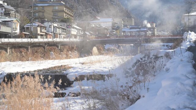 湯けむりが立ち上る雪景色の渋温泉街と横湯川の全景