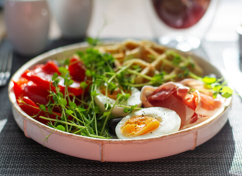 English breakfast. Boiled egg, jamon, waffles and green herbs.