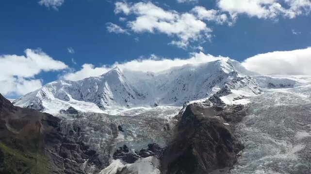 Snow-capped Himalayan mountain range with expansive glacier under bright blue sky and scattered clouds