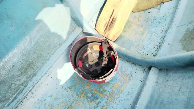 A red safety helmet resting inside a blue fiberglass boat with a wooden oar.