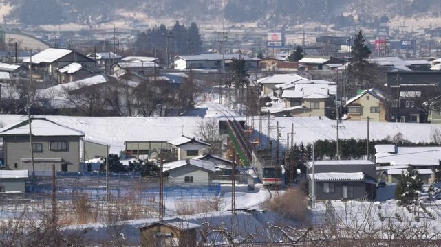 雪に覆われた冬の集落を走り抜ける長野電鉄の特急ゆけむり（1000形）