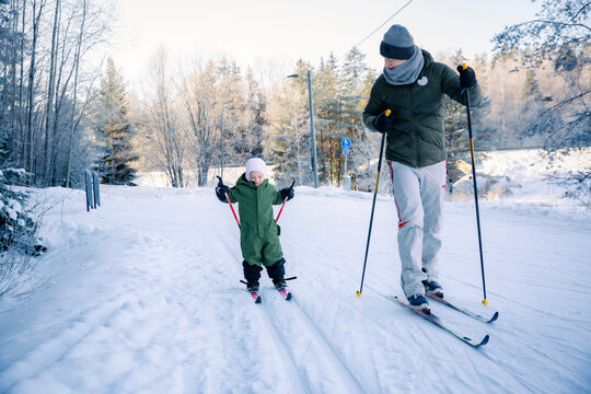 A father helps his toddler learn cross-country skiing on a snowy trail in Helsinki region, Finland, during an active winter family outing.