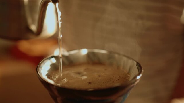Close up of a person brewing coffee using the pour over method in a warm, inviting kitchen. Hot water from a gooseneck kettle is poured over fresh grounds in a filter dripper