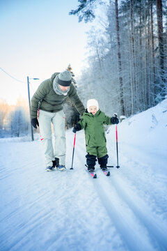 A father helps his toddler learn cross-country skiing on a snowy trail in Helsinki region, Finland, during an active winter family outing.